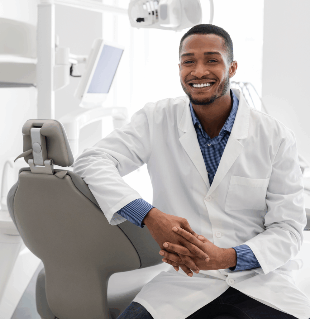 Dentist in office sitting on dental chair with equipment behind him.
