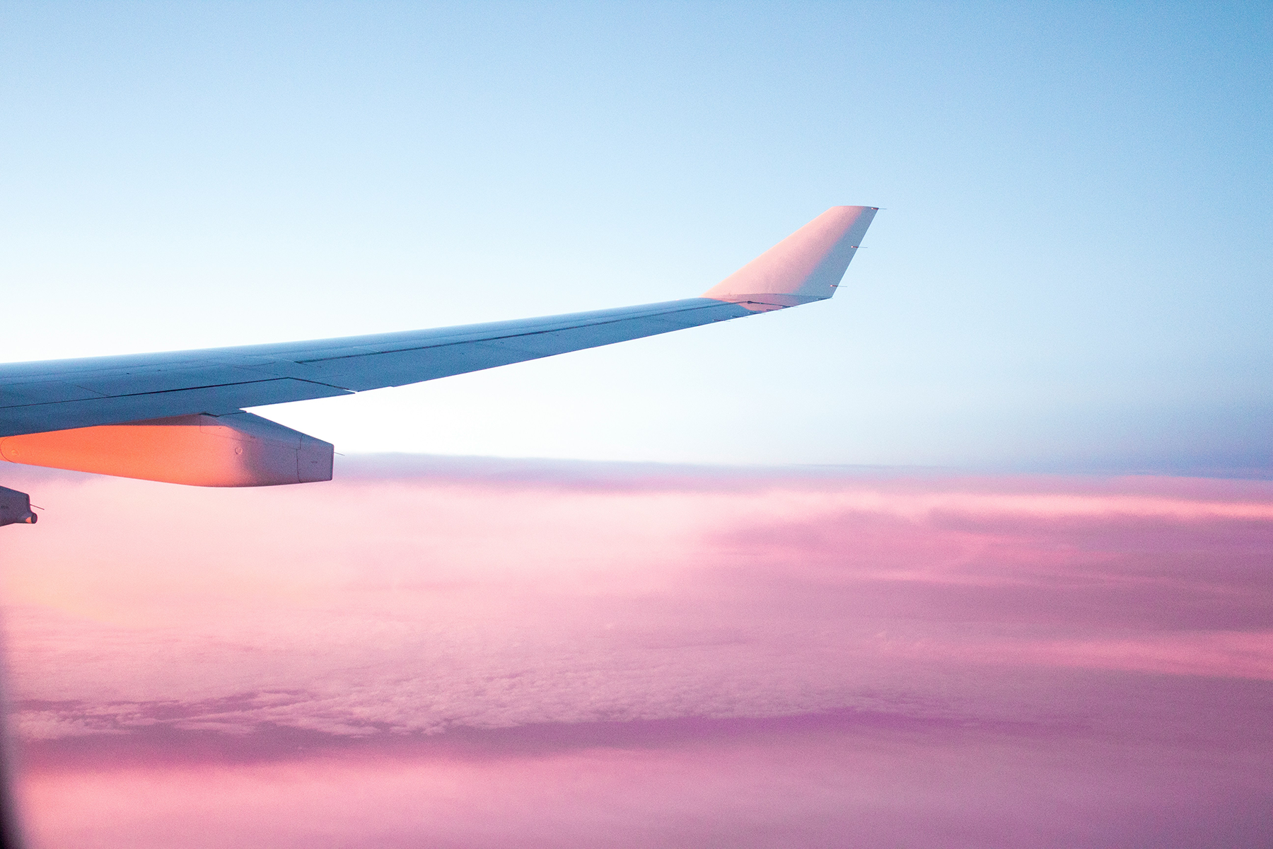Plane flying above clouds with pink and blue hues.